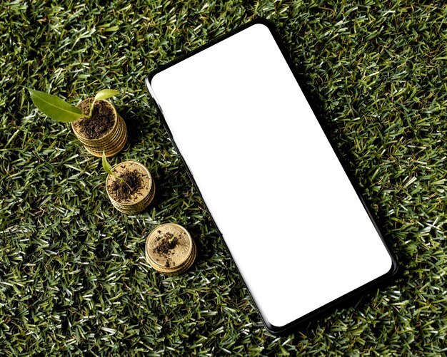 Vista dall'alto di tre pile di monete sull'erba con lo smartphone