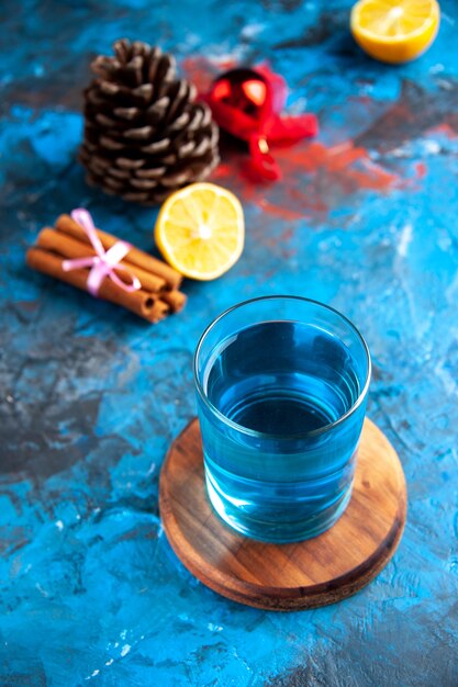 Vista dall'alto di un'acqua ferma in un bicchiere su tagliere di legno e limoni cannella lime cono di conifere su sfondo blu