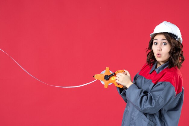 Vista dall'alto di un architetto donna scioccato in uniforme con nastro di misurazione di apertura del casco su sfondo rosso isolato