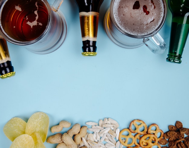 Vista dall'alto di un bicchiere di birra e una bottiglia con mix di snack salati sul blu con spazio di copia