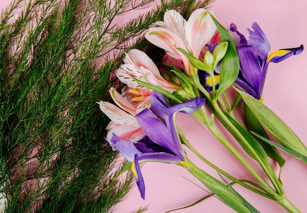 Vista dall'alto di un bouquet di iris viola scuro e fiori di alstroemeria con asparagi su sfondo rosa