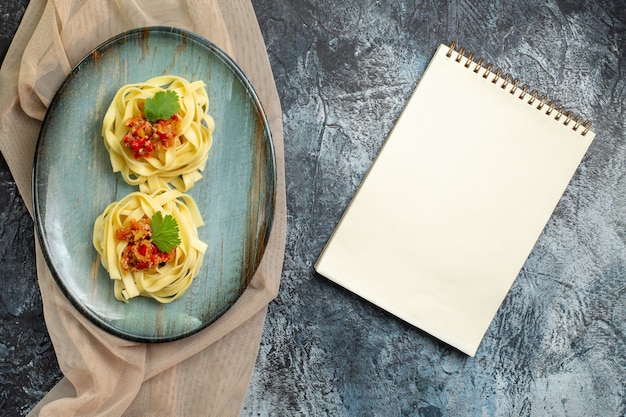 Vista dall'alto di un delizioso pasto di pasta su un piatto blu servito con pomodoro e carne per cena su un asciugamano color marrone chiaro accanto al notebook chiuso