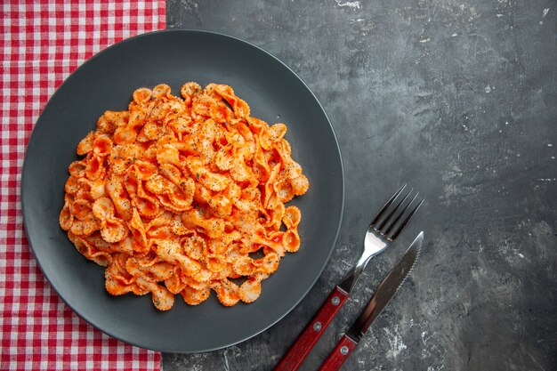 Vista dall'alto di un delizioso pasto di pasta su un piatto nero per cena su un asciugamano spogliato rosso e posate su sfondo scuro