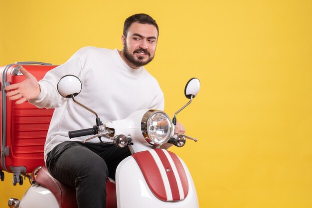 Vista dall'alto di un giovane curioso seduto in moto con la valigia sopra su sfondo giallo isolato