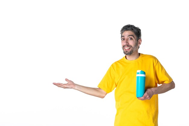 Vista dall'alto di un giovane maschio sorridente fiducioso in camicia gialla e che mostra thermos blu che punta qualcosa sul lato destro su sfondo bianco