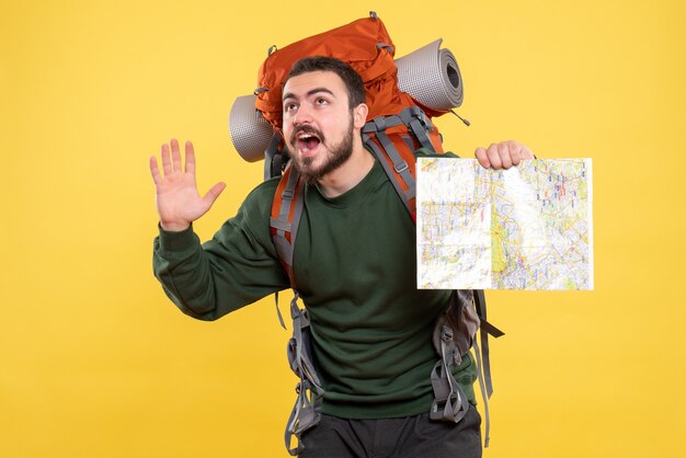 Vista dall'alto di un giovane ragazzo in viaggio sorridente con uno zaino che tiene in mano una mappa e mostra cinque su giallo