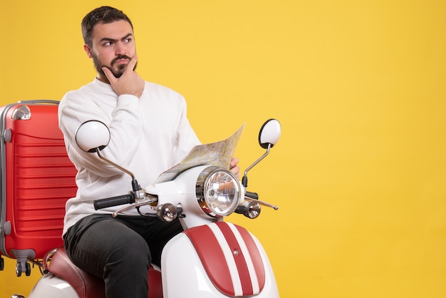 Vista dall'alto di un giovane ragazzo seduto in moto con la valigia sopra che si sente confuso su sfondo giallo isolato