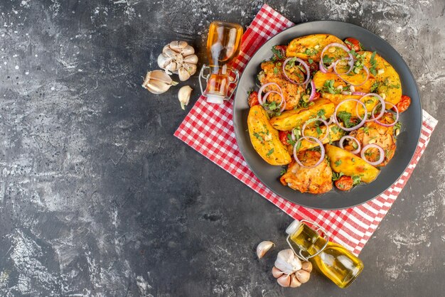 Vista dall'alto di un gustoso pasto di pollo con patate e verdure verdi su un asciugamano rosso spogliato bottiglie di olio cadute sul lato sinistro sul tavolo di colore scuro