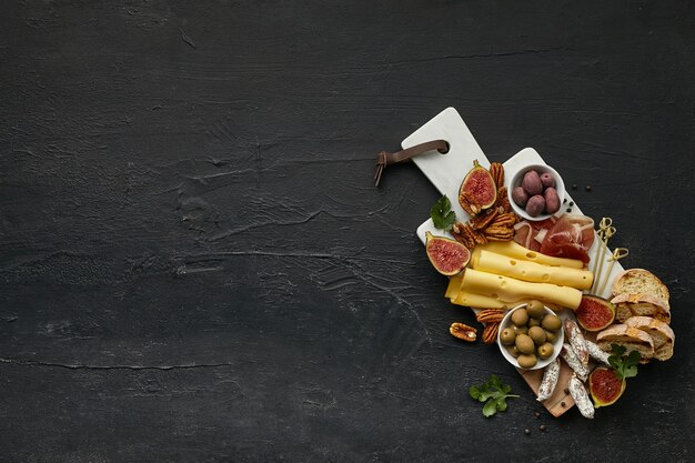 Vista dall'alto di un gustoso piatto di formaggi con frutta, uva, noci, olive e pane tostato sulla scrivania nera.