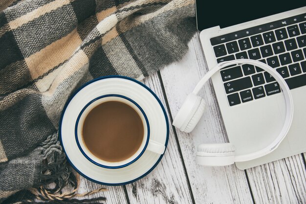 Vista dall'alto di un laptop moderno con cuffie wireless bianche e una tazza di caffè sul tavolo