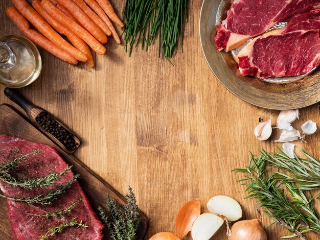 Vista dall'alto di un pezzo di carne rossa su tavola da cucina in legno e due pezzi di controfiletto su un piatto vintage. Copia spazio disponibile.