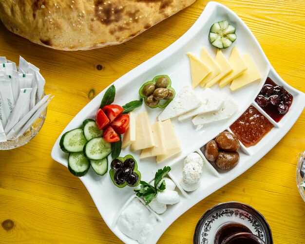 Vista dall'alto di un piatto con cibo per la colazione con verdure fresche olive formaggio miele e marmellata servito con tè