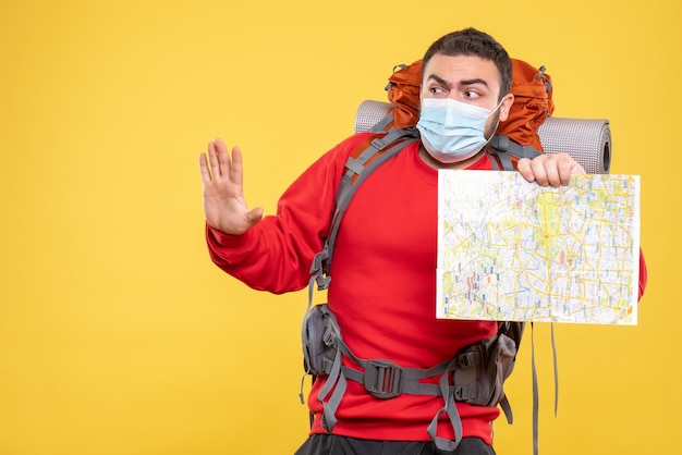 Vista dall'alto di un viaggiatore confuso che indossa una maschera medica con lo zaino che tiene la mappa che mostra cinque su sfondo giallo