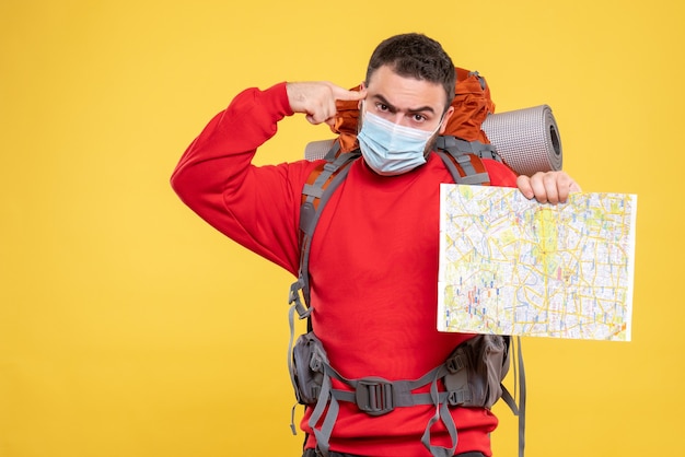 Vista dall'alto di un viaggiatore emotivo premuroso che indossa una maschera medica con zaino che tiene mappa su sfondo giallo