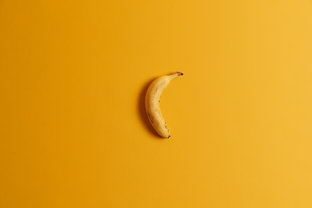 Vista dall'alto di una banana matura isolata su sfondo giallo. Deliziosa frutta tropicale per la tua gustosa colazione o spuntino. Pronto da mangiare banana intera. Utile prodotto nutriente ricco di vitamine