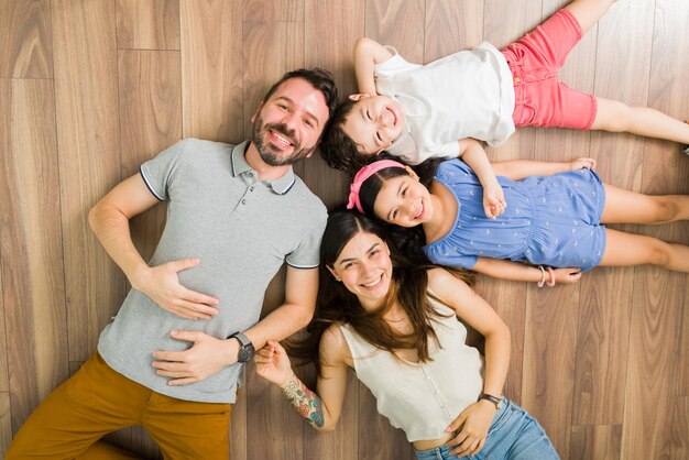 Vista dall'alto di una bella famiglia di quattro persone che si rilassano a casa e si divertono insieme. Bambina e ragazzo sdraiato sul pavimento con i loro genitori amorevoli