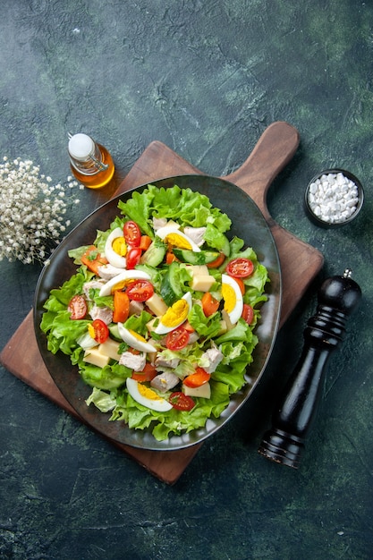 Vista dall'alto di una deliziosa insalata con molti ingredienti freschi sul tagliere di legno bottiglia di olio di sale su sfondo di colori mix verde nero