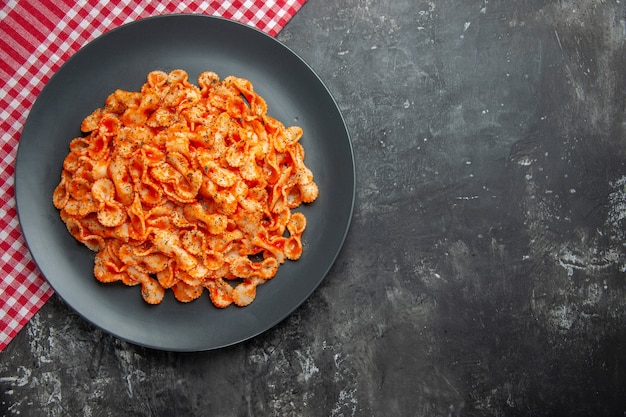 Vista dall'alto di una deliziosa pasta su un piatto nero per cena su un asciugamano spogliato rosso sul lato destro su sfondo scuro