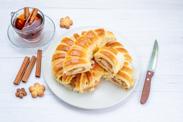 Vista dall'alto di una deliziosa pasticceria al forno con ripieno dolce affettato e intero insieme a biscotti e tè sulla scrivania luminosa, biscotto