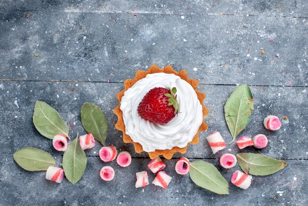 vista dall'alto di una deliziosa torta cremosa con fragole fresche e caramelle rosa a fette su grigio, torta dolce cuocere caramelle alla frutta crema