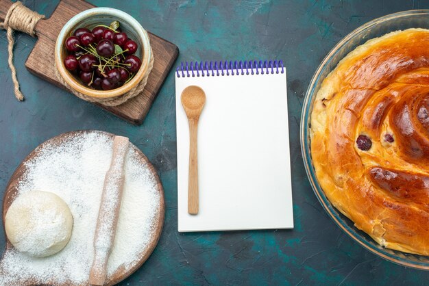 Vista dall'alto di una deliziosa torta di ciliegie con ciliegie di pasta blocco note su blu scuro, torta torta dolce zucchero cuocere