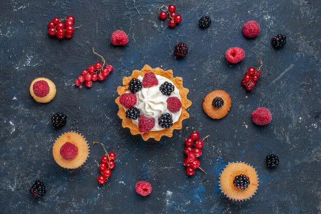 Vista dall'alto di una deliziosa torta dolce con diversi frutti di bosco e crema gustosa insieme a mirtilli rossi sparsi sulla scrivania scura, torta di frutti di bosco biscotto dolce