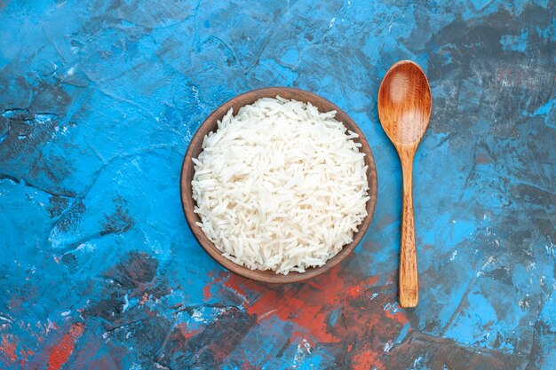 Vista dall'alto di una gustosa farina di riso in una piccola pentola marrone e un cucchiaio di legno sul tavolo blu