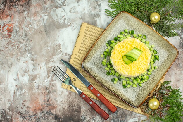 Vista dall'alto di una gustosa insalata servita con cetriolo tritato e forchetta per coltelli su un vecchio accessorio per la decorazione di giornali su sfondo a colori misti