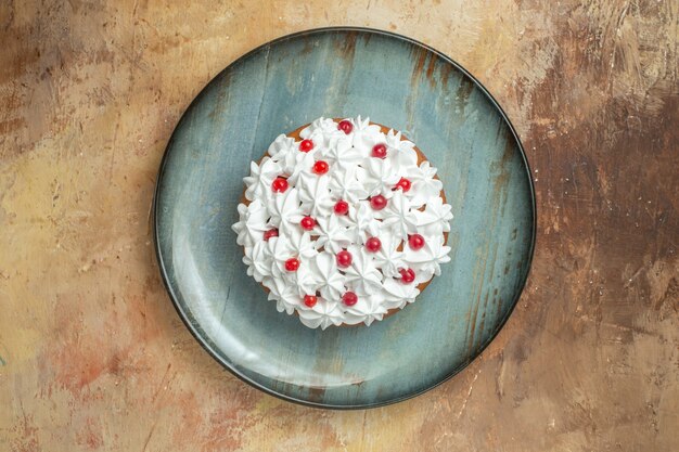 Vista dall'alto di una gustosa torta decorata con crema e ribes su un piatto blu su uno sfondo colorato