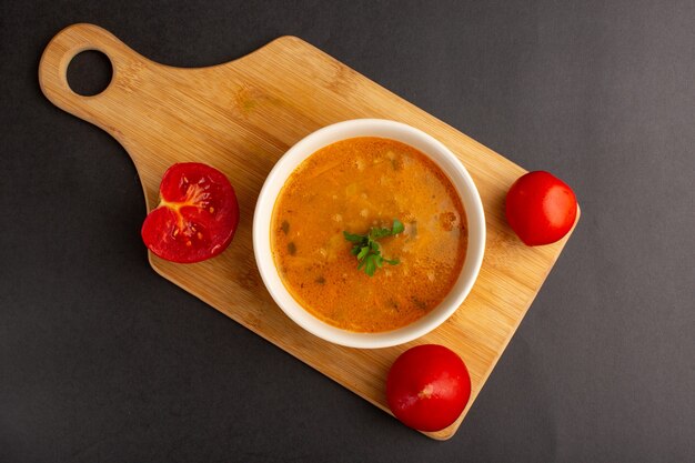 Vista dall'alto di una gustosa zuppa di verdure all'interno del piatto insieme ai pomodori sulla superficie scura
