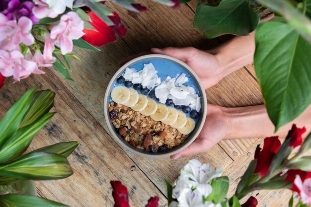 Vista dall'alto di una persona che tiene in mano una ciotola di frullato di mirtilli sana con frutta e muesli