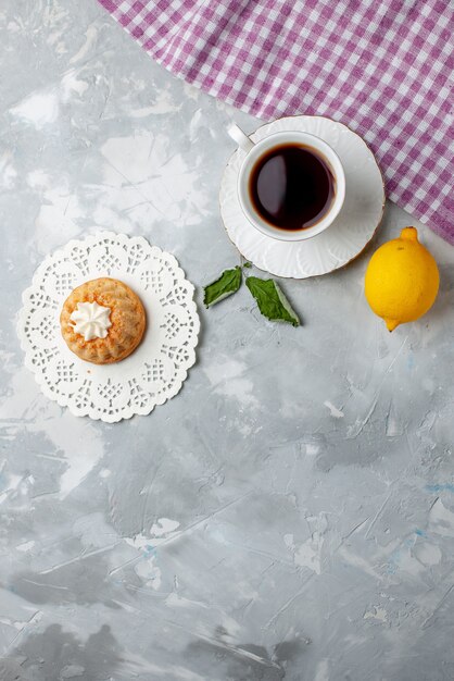 Vista dall'alto di una piccola torta deliziosa con tè e limone acido sulla scrivania leggera, biscotto torta biscotto dolce