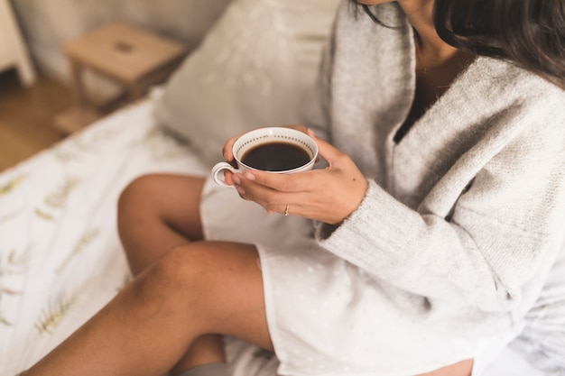 Vista dall&#39;alto di una ragazza che si siede sul letto che tiene tazza di caffè