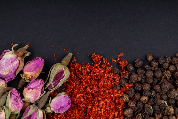 Vista dall'alto di una serie di spezie ed erbe tè rosa boccioli di peperoncino rosso fiocchi e pepe nero su sfondo nero