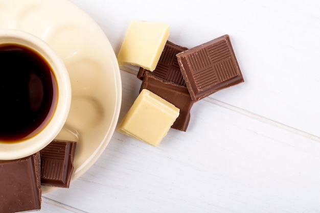 Vista dall'alto di una tazza di caffè con cioccolato bianco e fondente su fondo di legno bianco