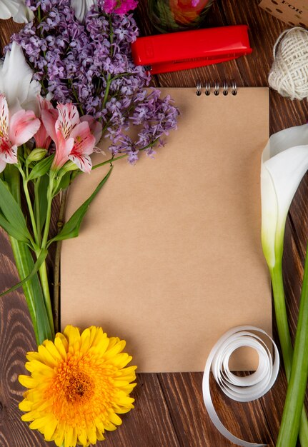 Vista dall'alto di uno sketchbook e bouquet di fiori primaverili di fiori e lillà rosa di alstroemeria su fondo di legno