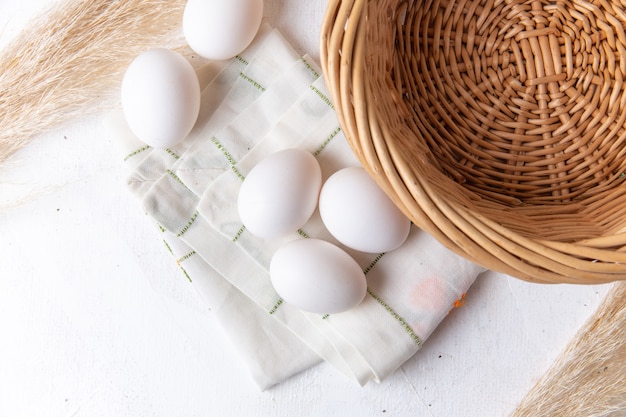 Vista dall'alto di uova intere bianche con cesto sulla superficie bianca