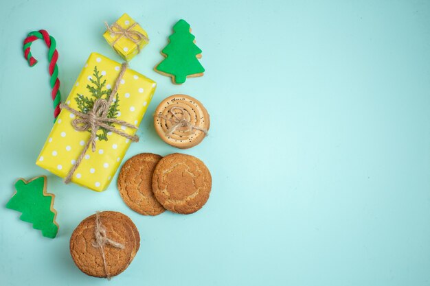 Vista dall'alto di vari biscotti di zucchero dell'albero di Natale e confezione regalo gialla su sfondo blu pastello