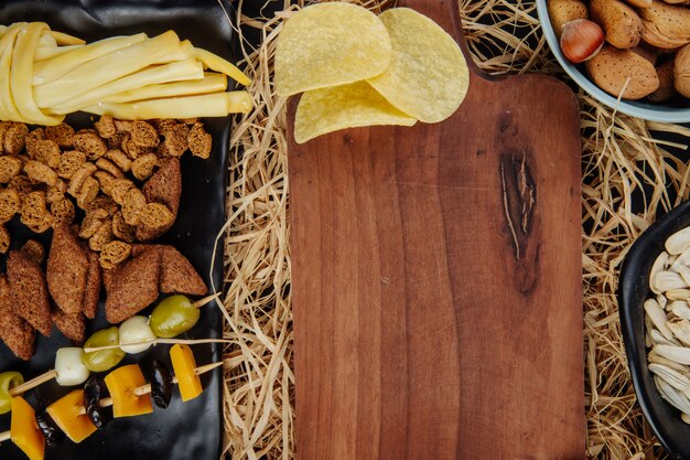 Vista dall'alto di vari spuntini di birra patatine fritte salamoia pane crackers e formaggio a pasta filata e un tagliere di legno sulla paglia