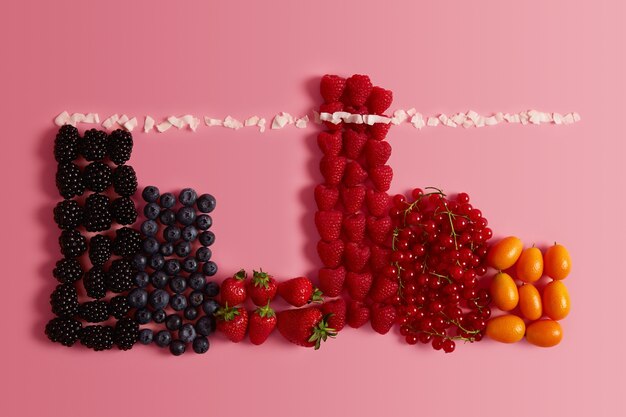 Vista dall'alto di varietà di deliziosi frutti estivi maturi. Frutti di bosco freschi sani. Mirtillo, mora, fragola, ribes e cumquat su sfondo rosa. Alimenti biologici, dieta e concetto di nutrizione