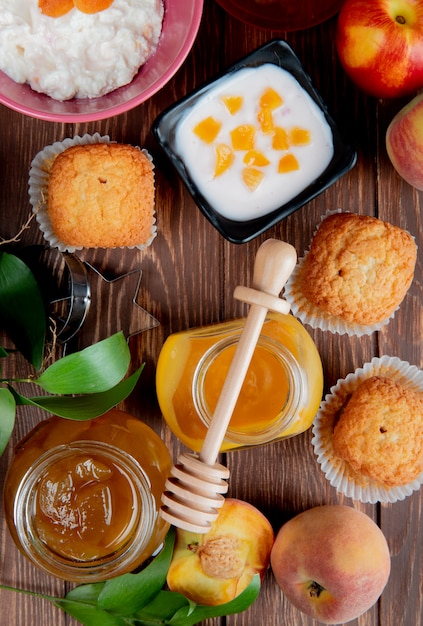 Vista dall'alto di vasetti di marmellate come pesca e prugne con ricotta cupcakes pesche su legno