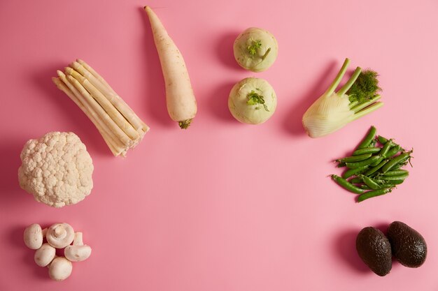 Vista dall'alto di verdure di stagione su sfondo rosa. Funghi freschi, broccoli, asparagi, ravanelli, finocchi, piselli e avocado maturo. Concetto di dieta sana. Copiare lo spazio al centro dell'inquadratura per il testo