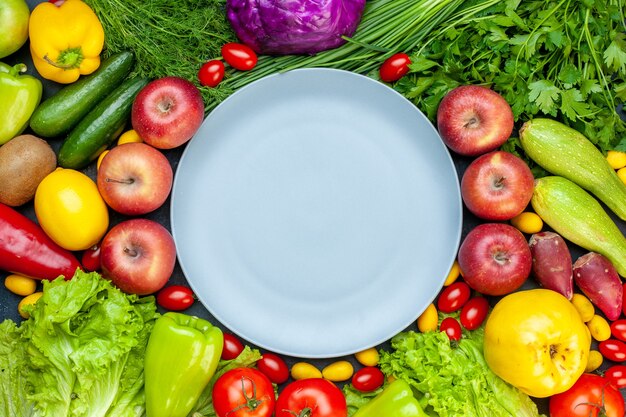 Vista dall'alto di verdure fresche pomodorini cumcuat ravanello cipolla verde prezzemolo cetrioli peperoni mele lattuga cavolo rosso piatto rotondo al centro