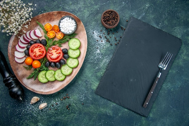 Vista dall'alto di verdure fresche tritate olive sale in una piastra marrone e cucina martello garlics forchetta sul tagliere di legno su sfondo verde nero colori misti