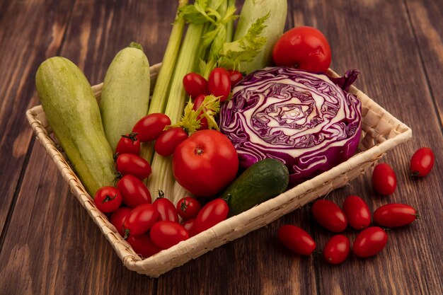 Vista dall'alto di verdure sane come pomodori sedano cavolo cappuccio viola e zucchine su un secchio su uno sfondo di legno