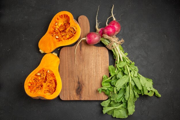 Vista dall'alto di zucca fresca con verdure e ravanelli su sfondo scuro