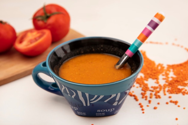 Vista dall'alto di zuppa di lenticchie arancione su una ciotola con cucchiaio con pomodori su una tavola di cucina in legno su una superficie bianca