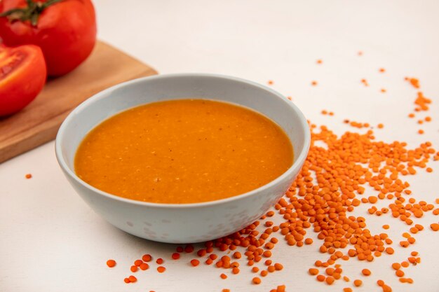 Vista dall'alto di zuppa di lenticchie arancione su una ciotola con i pomodori su una tavola da cucina in legno con lenticchie fresche isolato su una superficie bianca