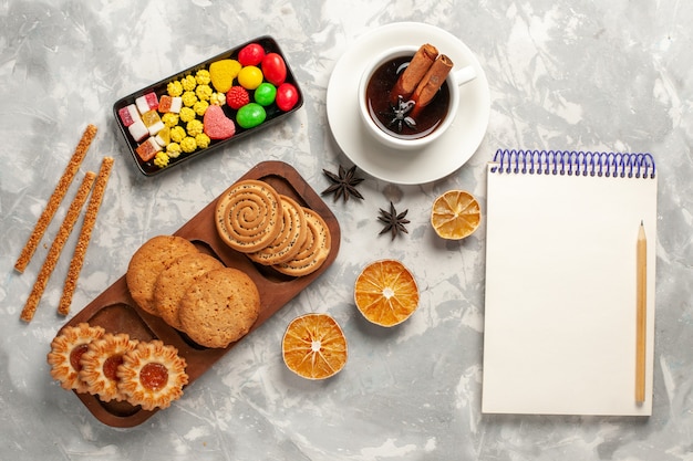 Vista dall'alto diversi biscotti con caramelle e tazza di tè su sfondo bianco biscotto biscotto zucchero cuocere torta torta dolce
