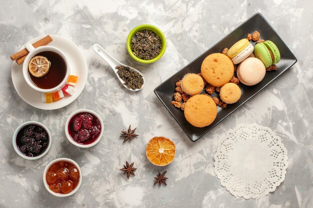 Vista dall'alto diversi biscotti con marmellate e tazza di tè sui biscotti dolci della torta di zucchero del biscotto della scrivania bianca